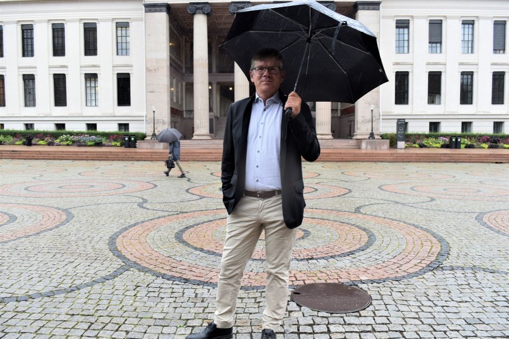 Ein mann med paraply står framfor Domus Media i sentrum
