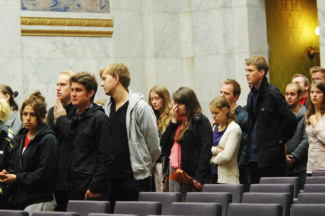 Fleire unge står i kø i Universitets aula.