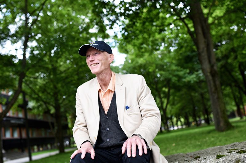 Thomas Hylland Eriksen sitter på en benk ute med en allé i bakgrunnen.