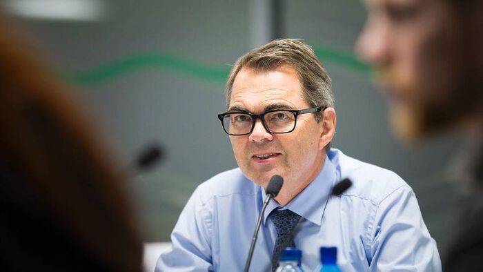 En mann med briller og blå skjorte sitter ved et møtebord