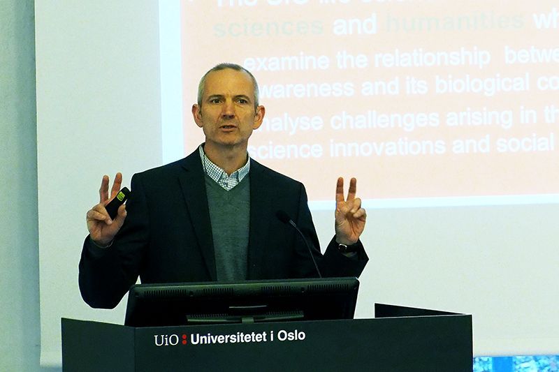 En mann står på talerstolen til Universitetet i Oslo og har begge armene delvis løftet
