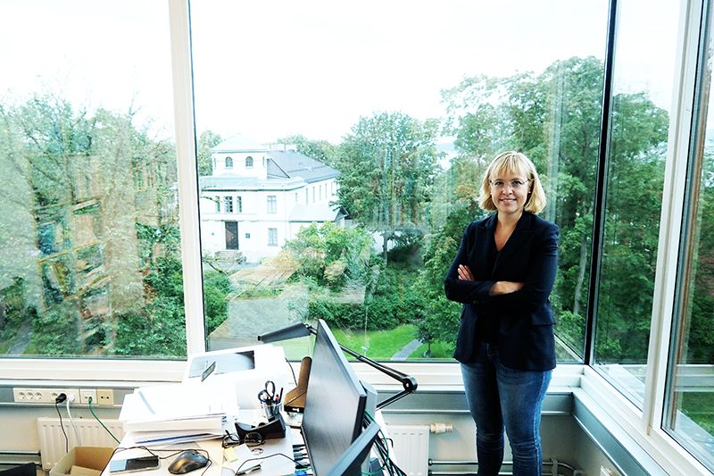 En kvinne står  på et kontor med vindusutsikt