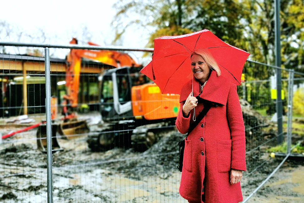 Kvinne med paraply står foran en byggeplass.