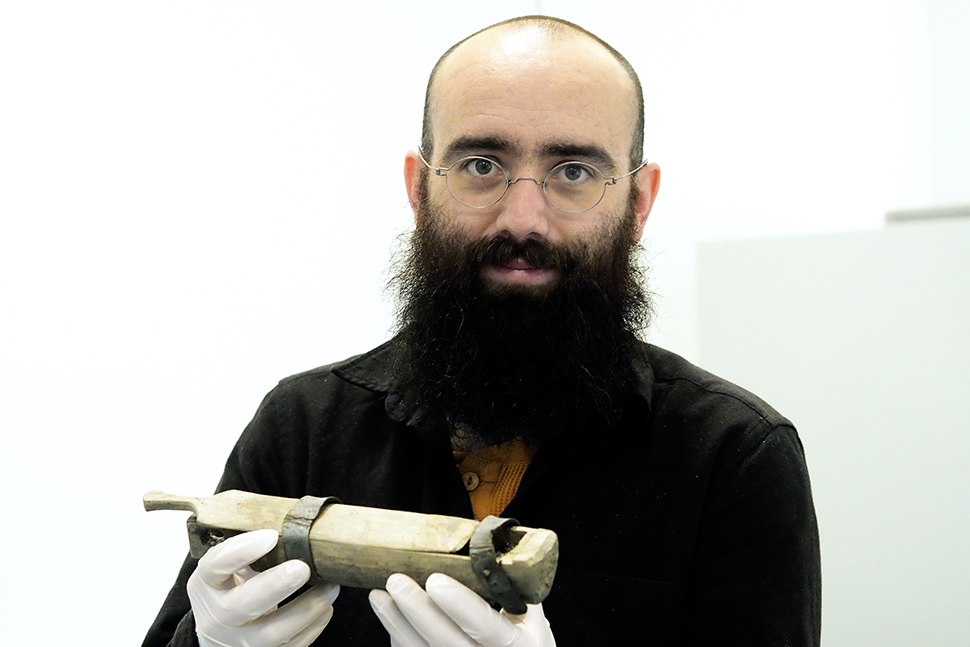 Ein mann med skjegg og lite hår viser fram eit 6000 år gammalt skrin av skinn og tre funne etter at ein isbre var smelta bort i Jotunheimen