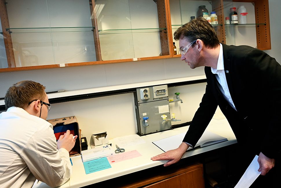 En mann får innføring i en kjemioppgave av en annen mann i et laboratorium