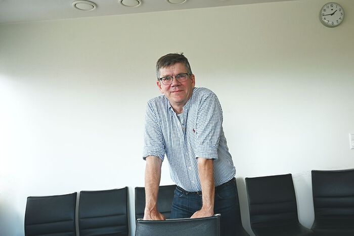 Ein mann står framfor ein stol og støttar seg med hendene på rygglenet