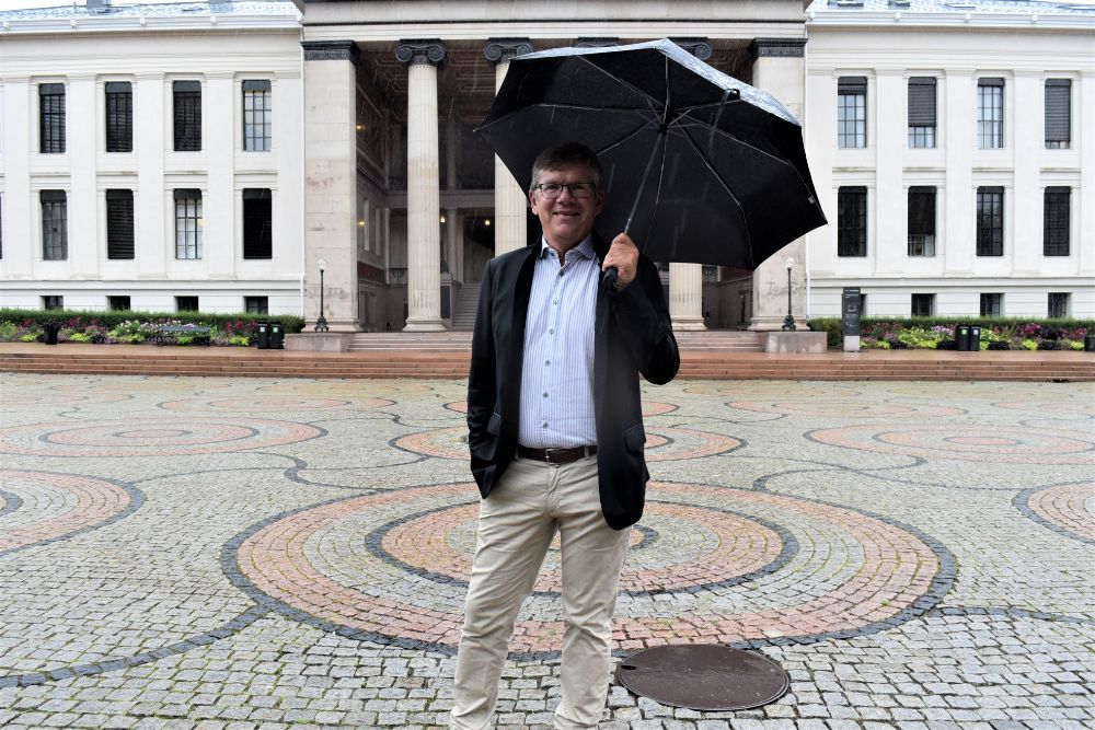 Ein mann med paraply står på Universitetsplassen