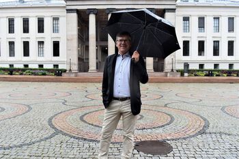 En mann med paraply står på Universitetsplassen