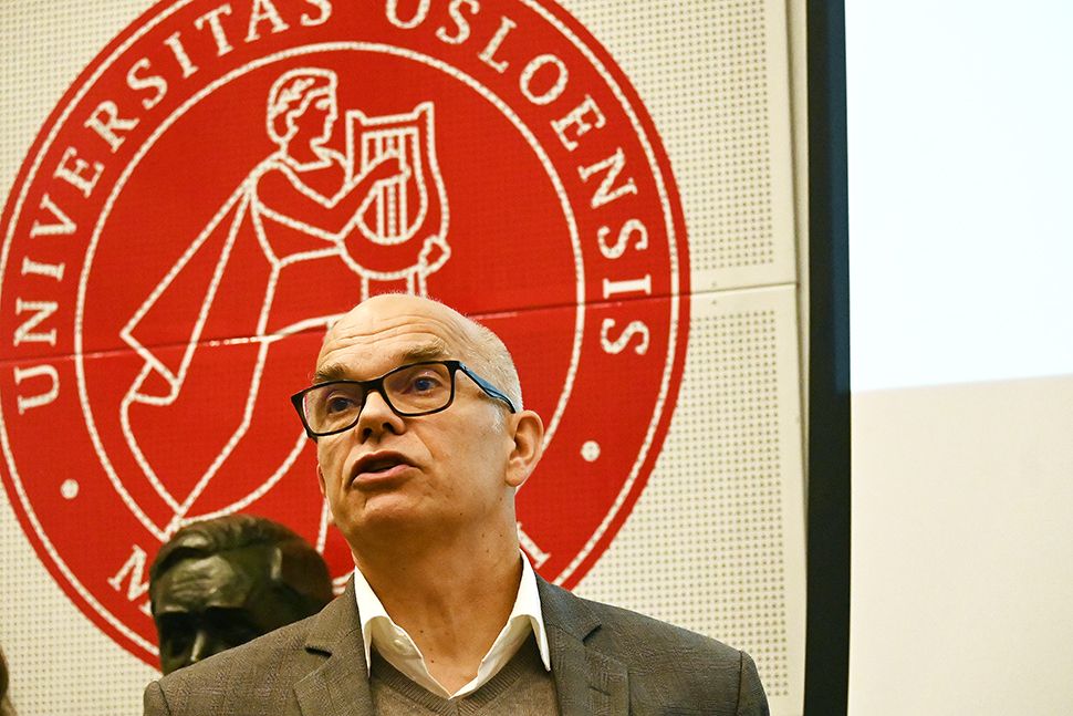 En mann med briller holder en tale foran logoen til Universitetet i Oslo