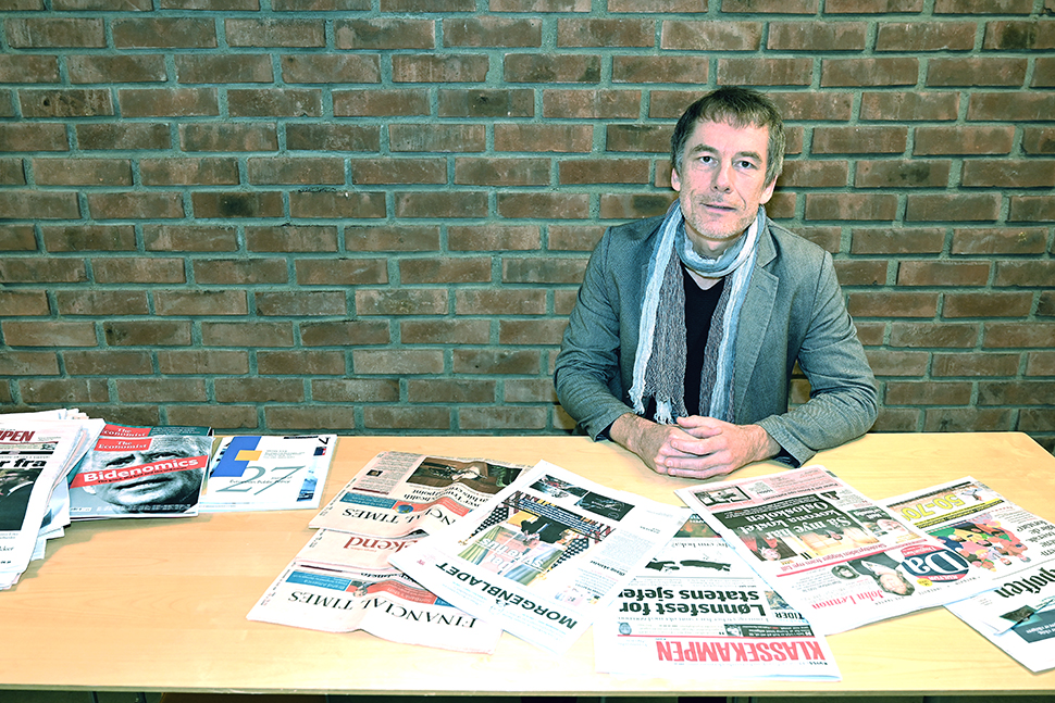 Portrett av en mann som sitter foran et bord med mange aviser