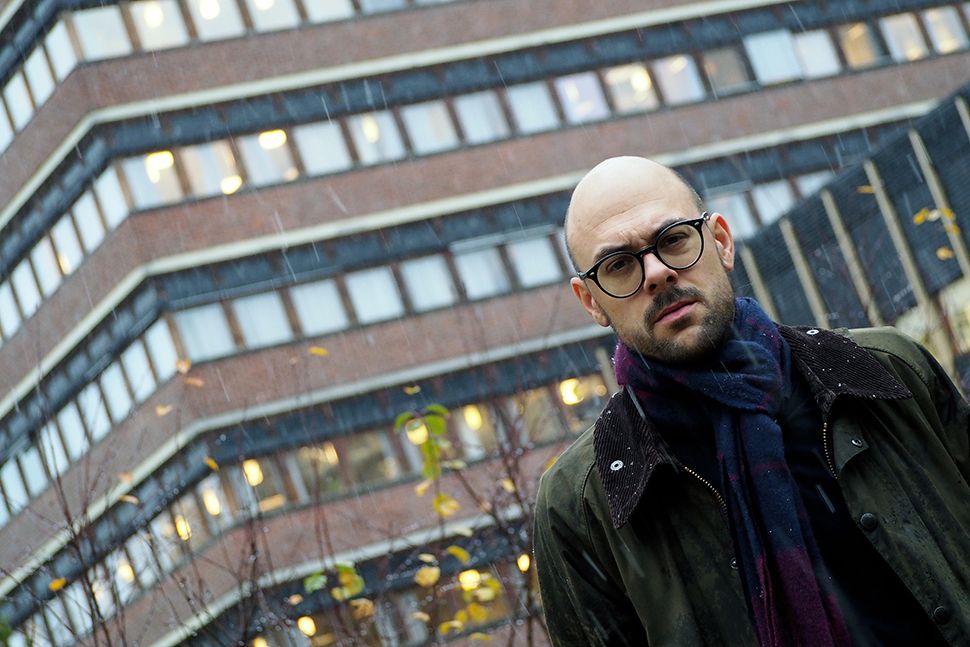 Ein mann utan hår, med briller står framfor ein høg bygning