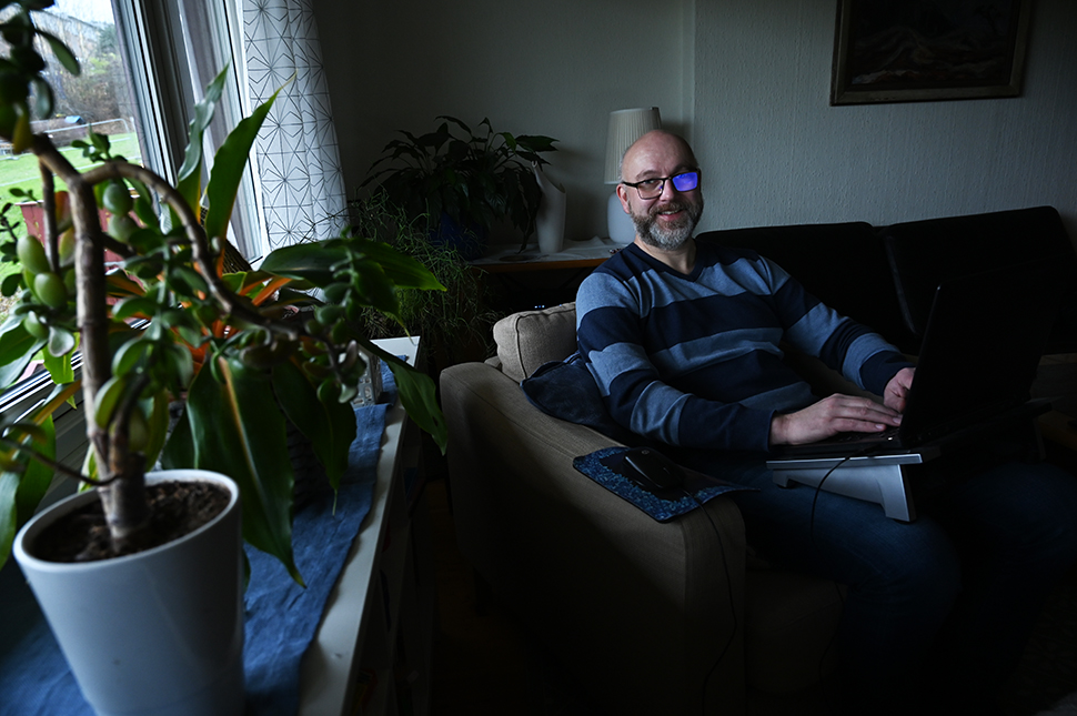 Ein mann sit i sofakroken med ei berbar datamaskin på fanget
