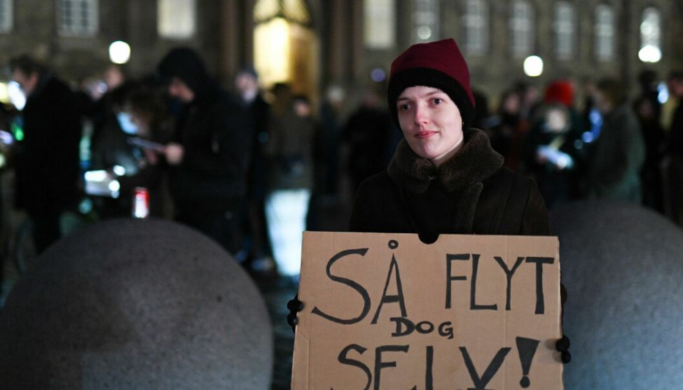 En kvinne står i en gate i København med en protestplakat