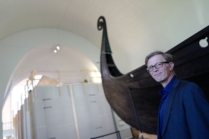 Portrett av ein mann med briller framfor eit vikingskip