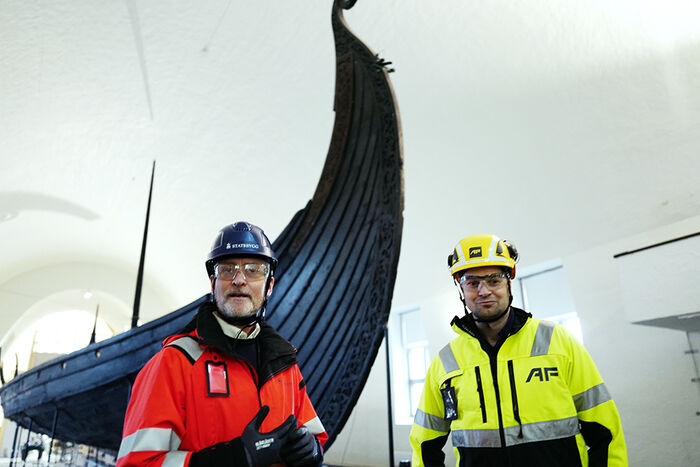 To menn med verneutstyr står framfor eit vikingskip