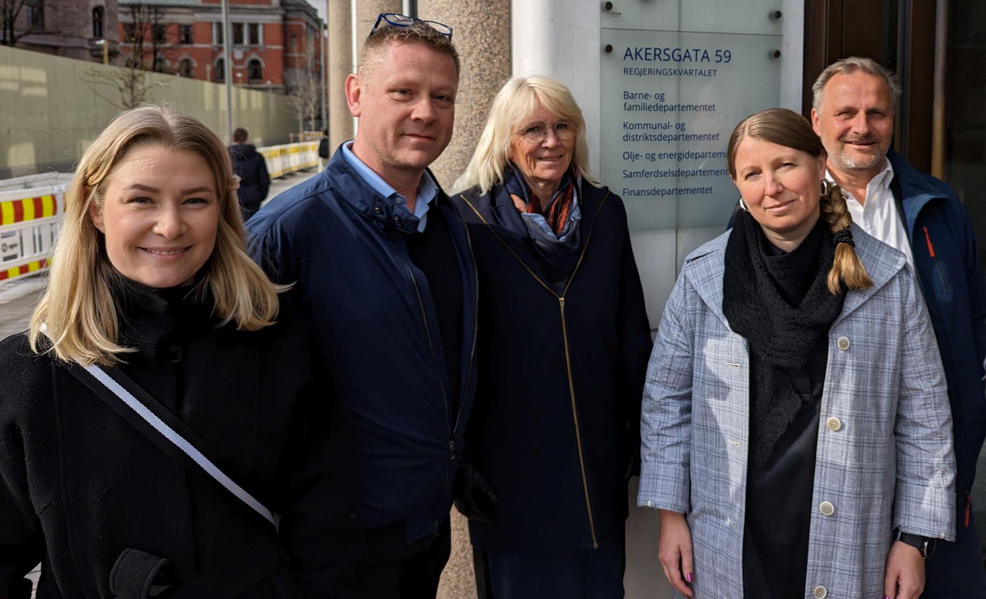 To menn og tre kvinner utenfor en departementsbygning