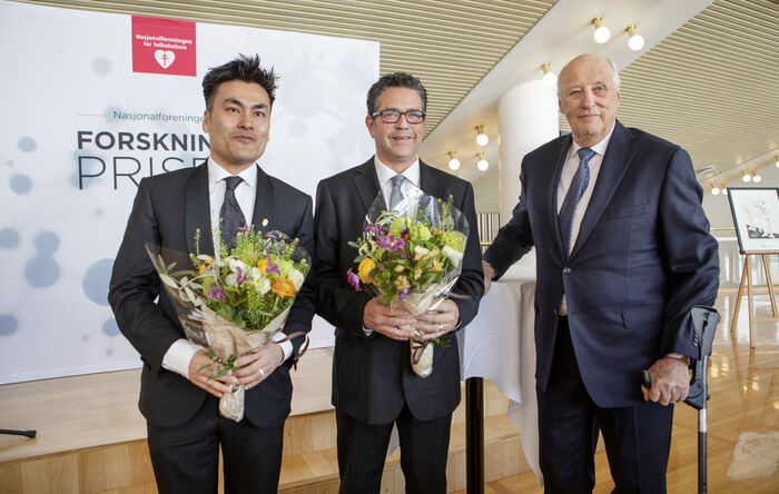 Tre menn står sammen, to av dem med blomster